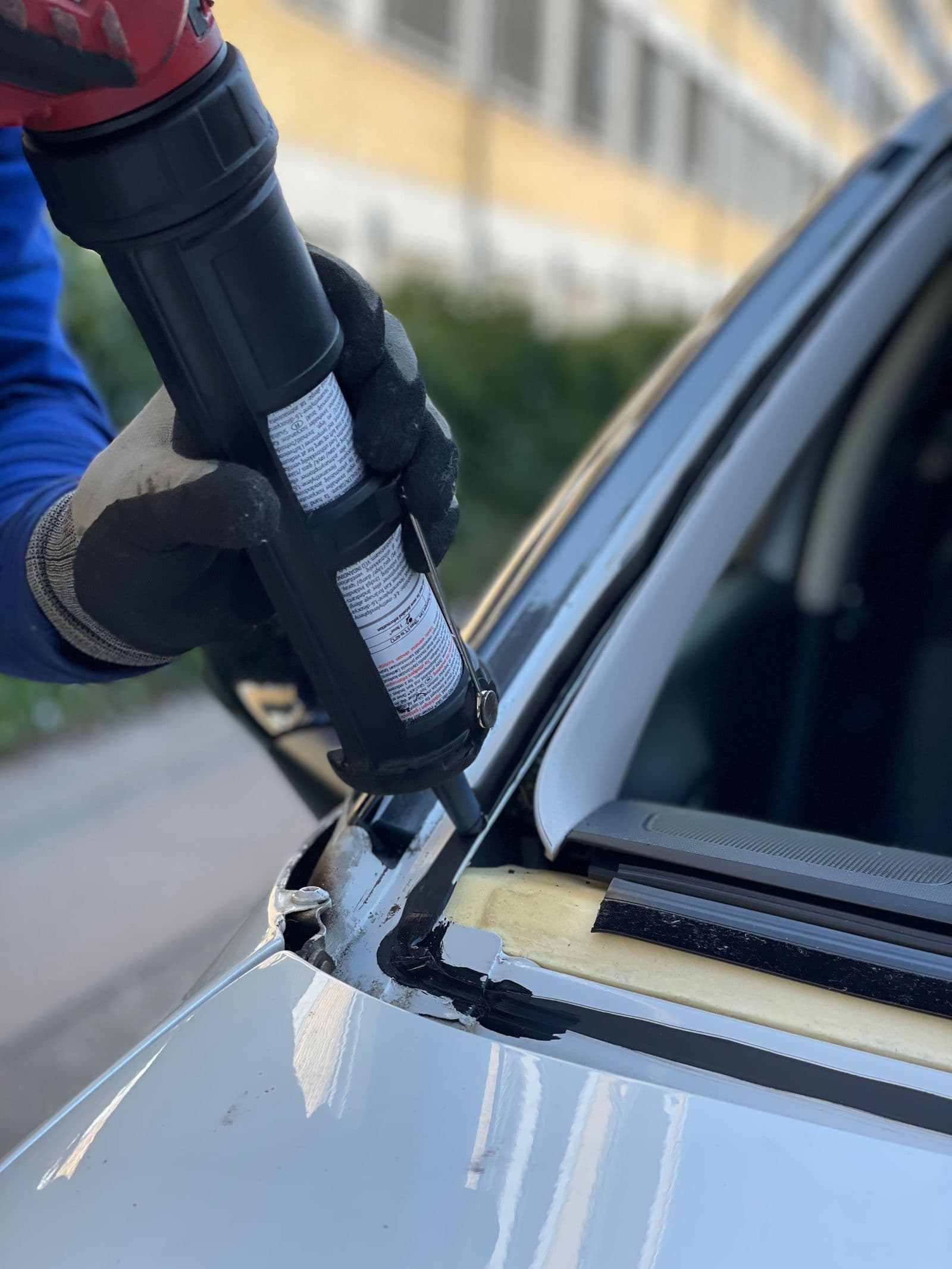 Technician applying urethane sealant around a windshield during installation